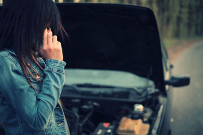 Side view of woman talking on phone against car on road