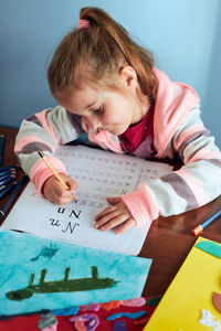 Little girl preschooler learning to write letters at home. kid using crayons doing homework