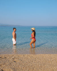 Rear view of woman standing at beach against clear sky