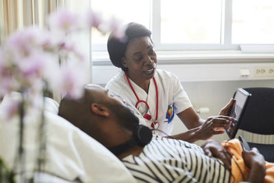 Mature practitioner showing digital tablet to male patient during routine visit in hospital