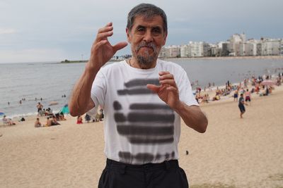 Portrait of senior man standing at beach against sky