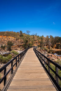 Footbridge amidst trees against blue sky