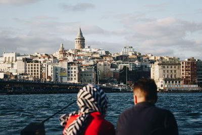 Rear view of man and boat in sea against buildings in city