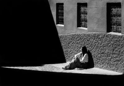 Full length of woman sitting on footpath by wall