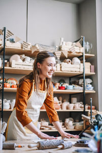 Smiling woman potter in her workshop, rolling out clay