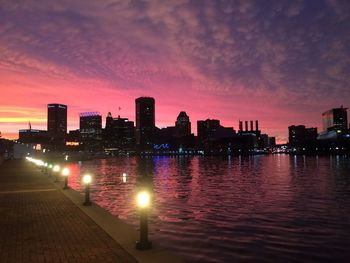 Illuminated footpath by lake in city against sky at dusk