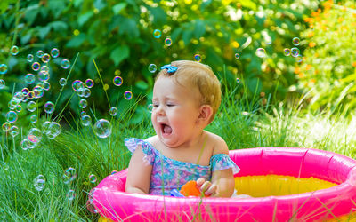 Cute girl sitting in wading pool looking at bubbles
