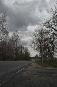 Road sign by trees against sky