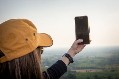 Man photographing with mobile phone against sky