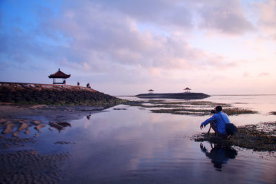 Man sitting on beach against sky during sunset