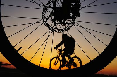 Silhouette man riding bicycle against sky seen through spokes