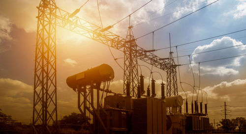 Low angle view of electricity pylons against sky during sunset