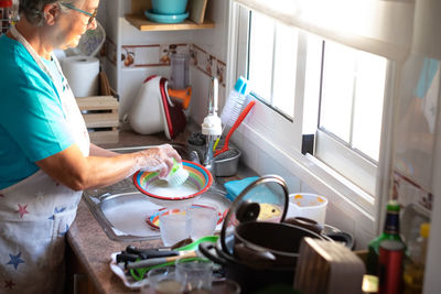 Senior woman cleaning dish at kitchen sink