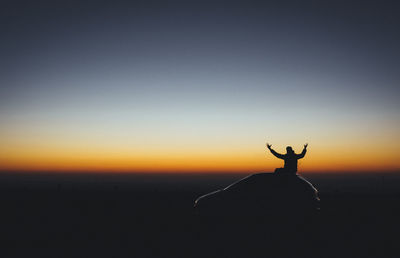 Silhouette man with arms raised against sky during sunset