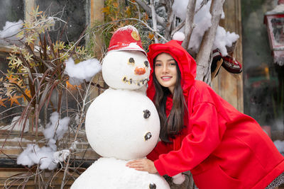 Portrait of young woman standing by snowman