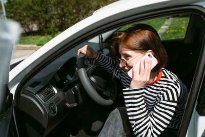 Portrait of a young brunette woman driving in a car using a smartphone