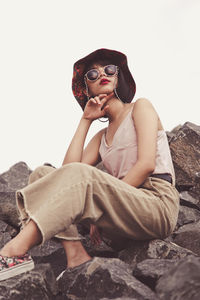 Low angle view of young woman sitting on rock against sky