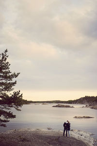 Rear view of couple standing at beach against sky during sunset