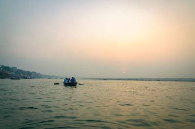 Rear view of people in boat on sea against sky during sunset