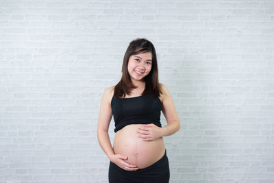 Portrait of smiling pregnant woman standing against wall