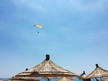 Low angle view of parachute flying over parasols against sky