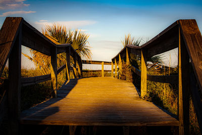 Empty boardwalk amidst plants against sky during sunset