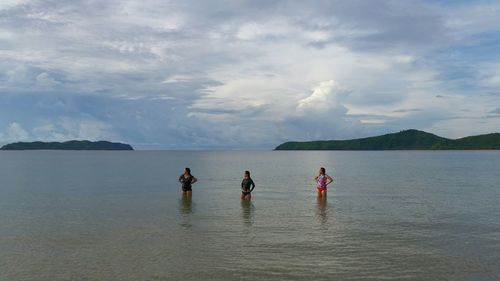 Women standing in sea against sky during sunset