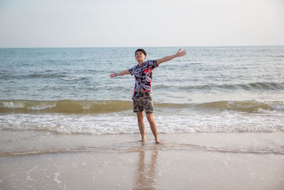 Smiling man with arms outstretched standing at beach against sky