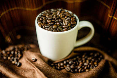 Close-up of roasted coffee beans with cup on fabric