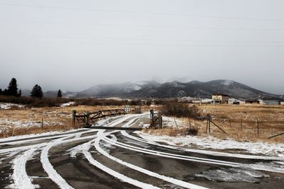 Snow covered road by mountain against sky