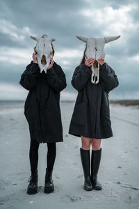 Full length of friends standing on umbrella against sky