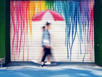 Blurred motion of woman walking against wall in city