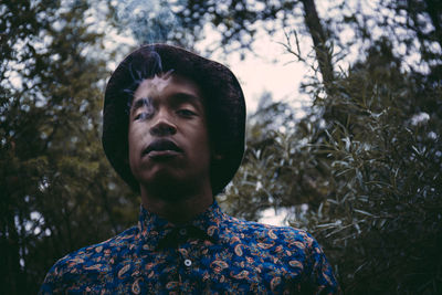 Portrait of man exhaling smoke against tree