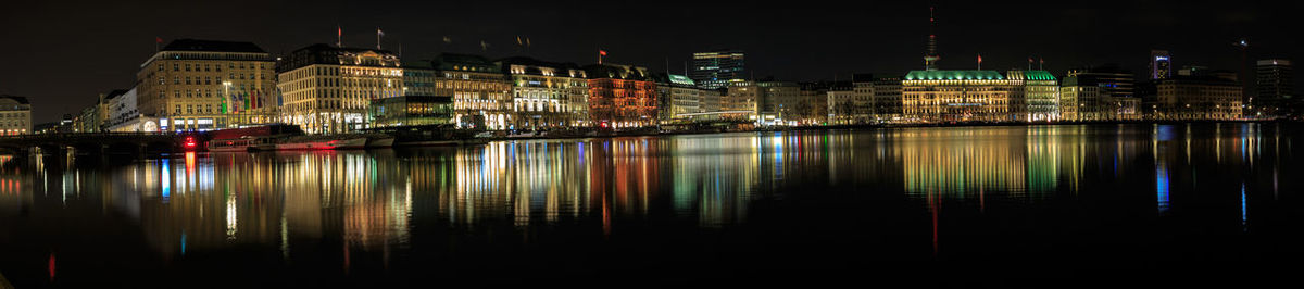 Illuminated buildings by river against sky at night
