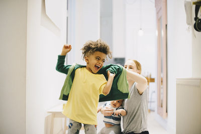 Mother with toddler dressing happy son at home