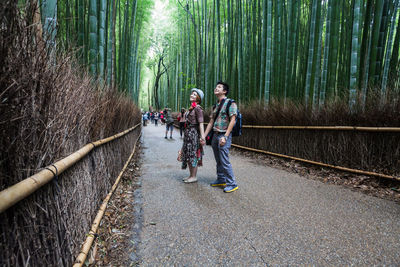 Smiling couple standing on pathway amidst bamboos at arashiyama