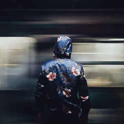 Rear view of person wearing floral pattern jacket standing against vehicle