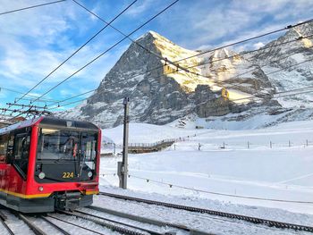 Overhead cable car on snow covered railroad tracks against sky