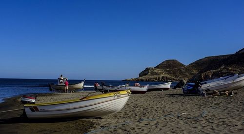 Boats moored on beach shore against clear blue sky