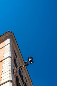 Low angle view of bird perching on building against blue sky