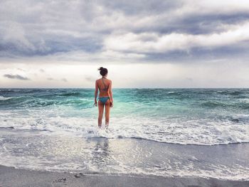 Rear view of women standing in front of sea against cloudy sky