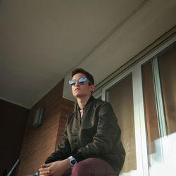 Low angle view of man wearing sunglasses looking away while sitting at home