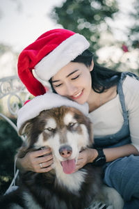 Smiling woman wearing santa hat with dog sitting outdoors