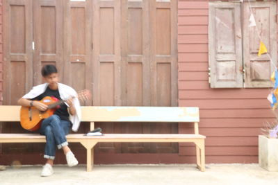Full length of man sitting on bench against building