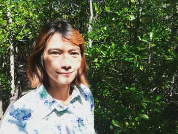 Portrait of smiling young woman standing against trees