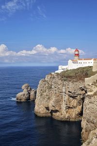 Lighthouse on cliff by sea against sky