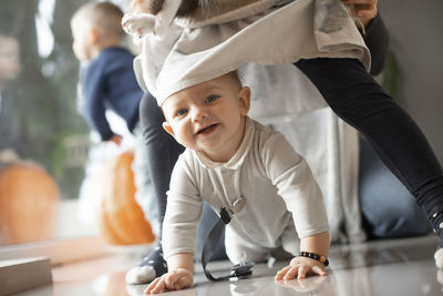 Smiling baby crawling on the floor between his sister's legs