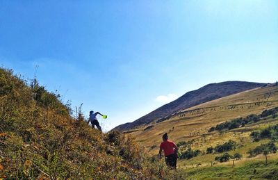 Rear view of woman walking on mountain against clear blue sky