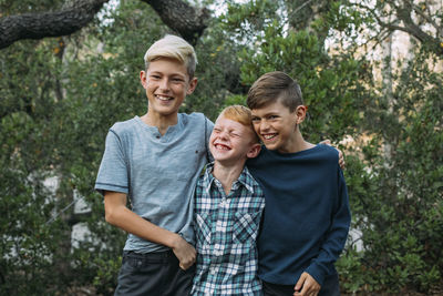 Happy brothers standing side by side against trees at park