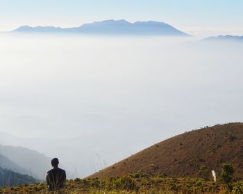 Rear view of man standing on mountain against sky